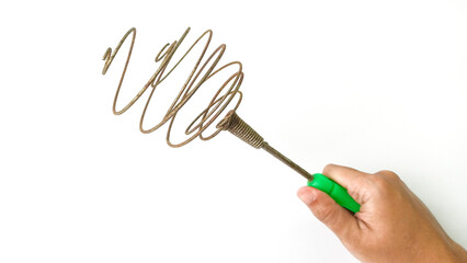 hand holding an antique metal coil egg whisk with a green handle, kitchen utensil on a white background. Used for cooking and baking.