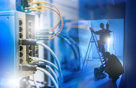 Technicians installing or maintaining network cables and hardware in server room with Ethernet switches. IT infrastructure, data center, telecommunications setup.