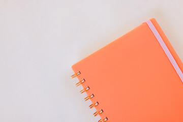 Bright orange notebook with pink elastic band sits on smooth, light colored surface, showcasing its vibrant design.