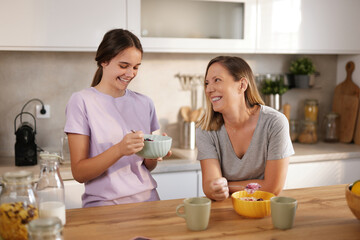 A mother and her daughter laugh and share a happy moment over breakfast. They enjoy bowls of cereal...