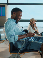 Happy tourist using smartphone in airport lounge while waiting for flight departure