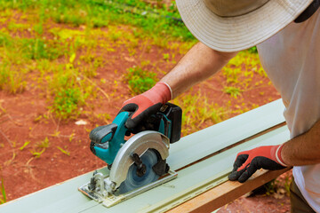 Carpenter is operating circular power saw on vinyl siding plank while working on construction...