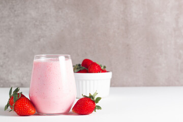 Glass of fresh strawberry milkshake, smoothie and fresh strawberries on white and wooden background. Healthy food and drink concept.