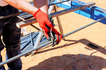Worker in gloves grips metal rebar with pliers while constructing steel rebar framework