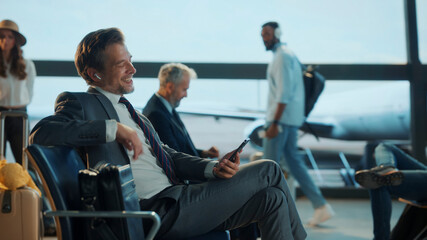 Smiling businessman using smartphone and earbuds in airport lounge