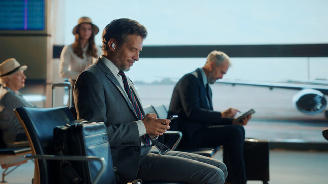 Businessman using smartphone and wearing earbuds in airport lounge