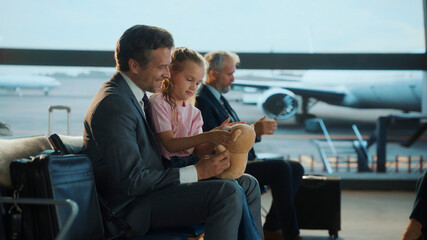 Business dad spends a heartfelt moment with his daughter at the airport, playing with her teddy...
