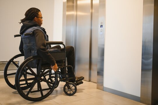 Young African American man in wheelchair waiting for elevator in modern building