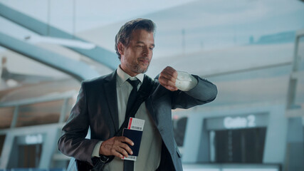 Businessman checking time at airport holding passport and boarding pass
