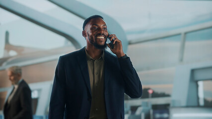 Smiling businessman talks on the phone while walking through airport terminal near Gate 2 —...