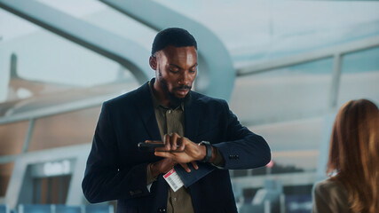 Businessman checking time in airport lounge while holding smartphone and passport
