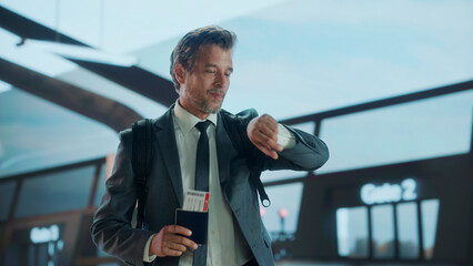 Business traveler with backpack checks his watch while holding passport and boarding pass at the...