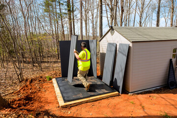 Worker installs large panels while standing on wooden platform during assembling storage shed...