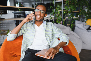 Smiling university student talking on phone and holding notebook in modern library