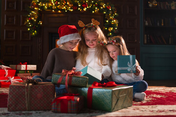 Merry Christmas Xmas holiday. Children unpacking open up gift box near Christmas tree. Kids in living room with Christmas tree fireplace opening gift box with surprise faces. Christmas eve at home