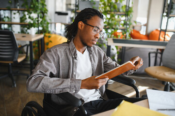 Focused student in wheelchair reading book in modern office