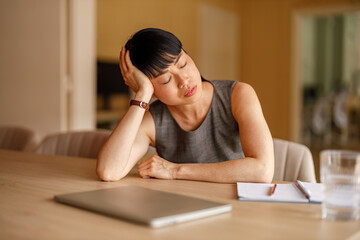 Exhausted female professional woman with head in hand sleeping by laptop at desk in corporate workplace