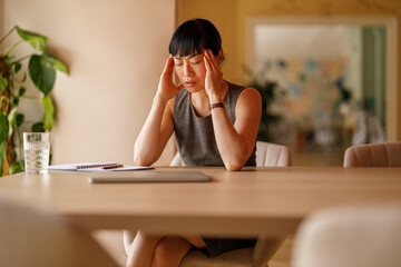 Stressed businesswoman with head in hands overwhelmed by workload and deadlines at corporate office desk