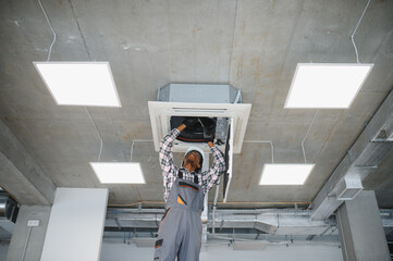 African American Technician repairing ceiling ventilation system in office