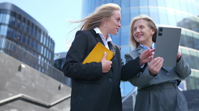 Young women in business attire collaboratively explore digital content on a tablet.