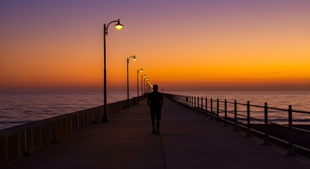 Lone person walking along a beachside promenade at sunset, with the sea reflecting the orange glow of the sun.