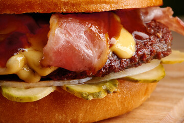 Delicious burger showing melted cheese, bacon, pickles, and onions on a wooden board