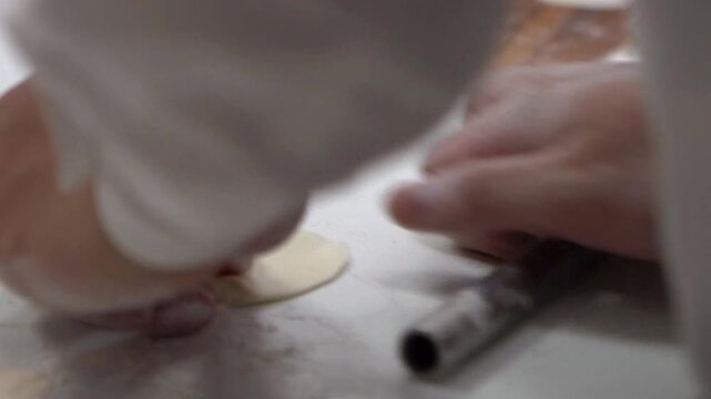 Slow motion of a Taiwanese culinary chef rolls out the dough, ready to fill it with seasoned meat for making jiaozi, a classic Chinese dumpling. An Asian man assembling dumplings in restaurant kitchen