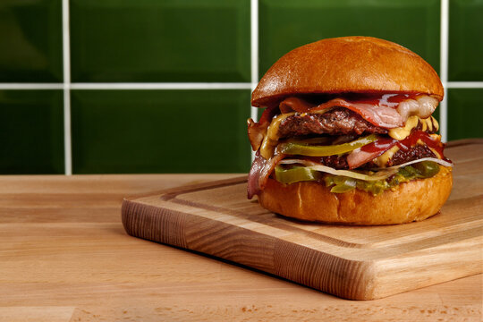 Delicious burger with bacon, cheese, and jalapenos sitting on wooden cutting board