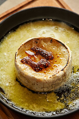 Delicious baked camembert cheese wheel covered with honey slowly melting in butter