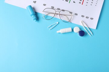 Vision test chart, glasses, tweezers, lenses and bottles of medical drops on light blue background, flat lay. Space for text