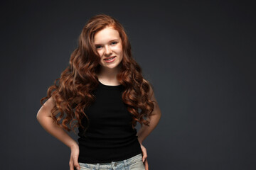 Portrait of smiling teenage girl with healthy wavy hair on dark grey background. Space for text