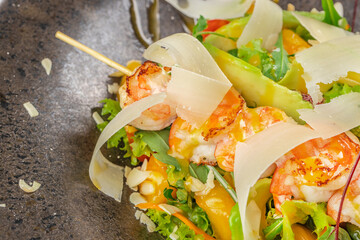 Grilled shrimp and parmesan shavings top a vibrant mixed salad with fresh greens, vegetables, and avocado slices for a gourmet seafood dish