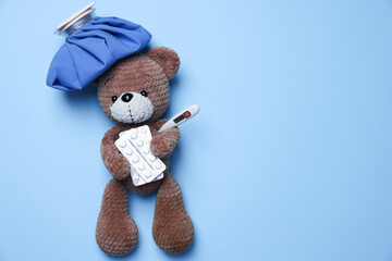 Pediatrics concept. Toy bear with ice bag, pills and thermometer on light blue background, top...