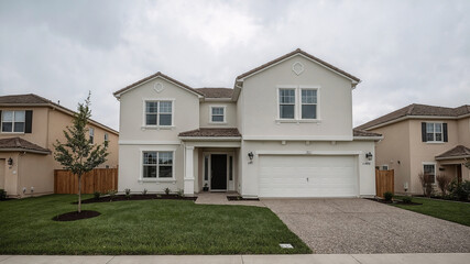 Modern two story house exterior on a cloudy day with a well manicured lawn and driveway with a focus on real estate and property ownership
