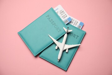 Passports with tickets and airplane model on pink background, top view