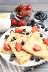 Delicious crepes with berries and cream on grey wooden table, closeup
