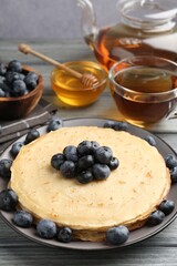 Delicious crepes with blueberries, honey and tea on grey wooden table, closeup
