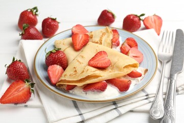 Delicious crepes with strawberries and cream on white wooden table, closeup
