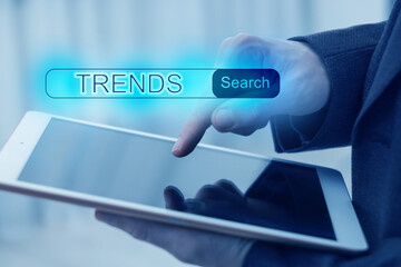 Businessman using tablet computer to find hot tendencies, new ideas, popular directions, closeup. Search bar with word Trends