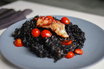 Close-up of exotic seafood risotto with octopus and tomato, black rice dish for culinary or menu...