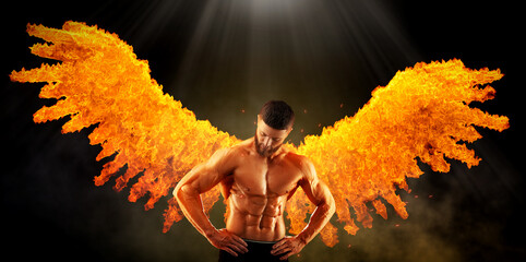 Bodybuilder with flaming wings behind his back against dark background. Shirtless muscular man