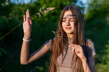 Teen Girl with Grass Shadow on Face. Young girl standing outdoors with closed eyes, holding dry...