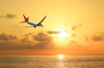 Airplane flying above sea in beautiful sky with clouds at sunset