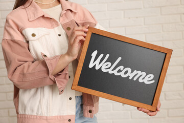 Woman holding small chalkboard with word Welcome indoors, closeup