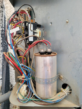 Air conditioner intricate bundle of multicolored dusty zip-tied electric wires along with a securely strapped run capacitor and a contactor fixed above it
