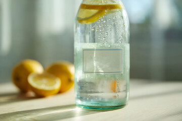 Chilled Glass Bottle with Lemon Slices and Sparkling Water on Sunlit Table with Fresh Lemons in Background
