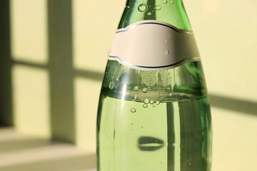 Chilled Green Glass Bottle with Blank Label and Sparkling Water in Bright Sunlight Casting Shadows on Light Background