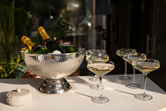 A Glamorous Display of Sparkling Wine Bottles and Elegant Champagne Coupes on a Marble Table Surrounded by Lush Greenery in a Sophisticated Setting
