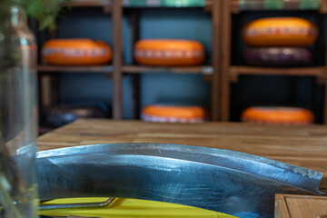 Large curved cheese knife and wooden table in foreground with blurred shelves displaying numerous...