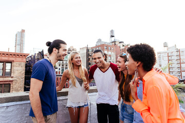 Cheerful young multi-ethnic friends toasting drinks while enjoying a vibrant rooftop party in new york city, surrounded by delicious food, laughter, and the stunning skyline